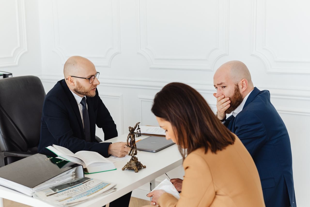 The Art of Drawing Readers In: Your attractive post title goes here A serious legal consultation in a professional office environment involving three adults.